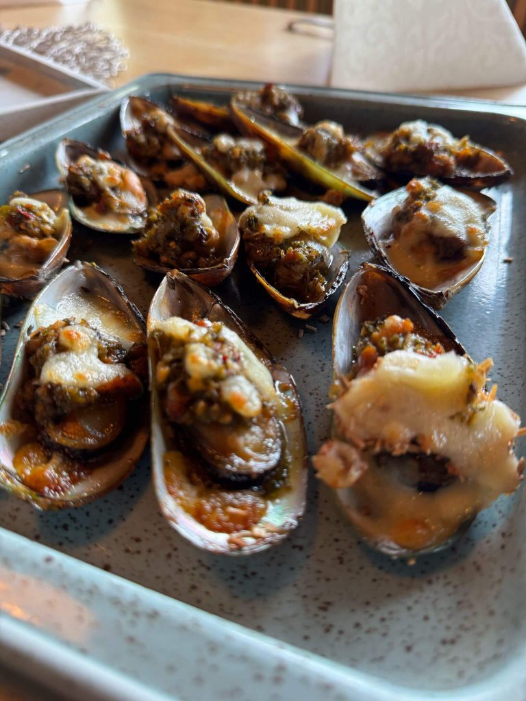 Gegrillte Muscheln mit Käse auf Teller als regionale Spezialität und lokale Wirtschaft